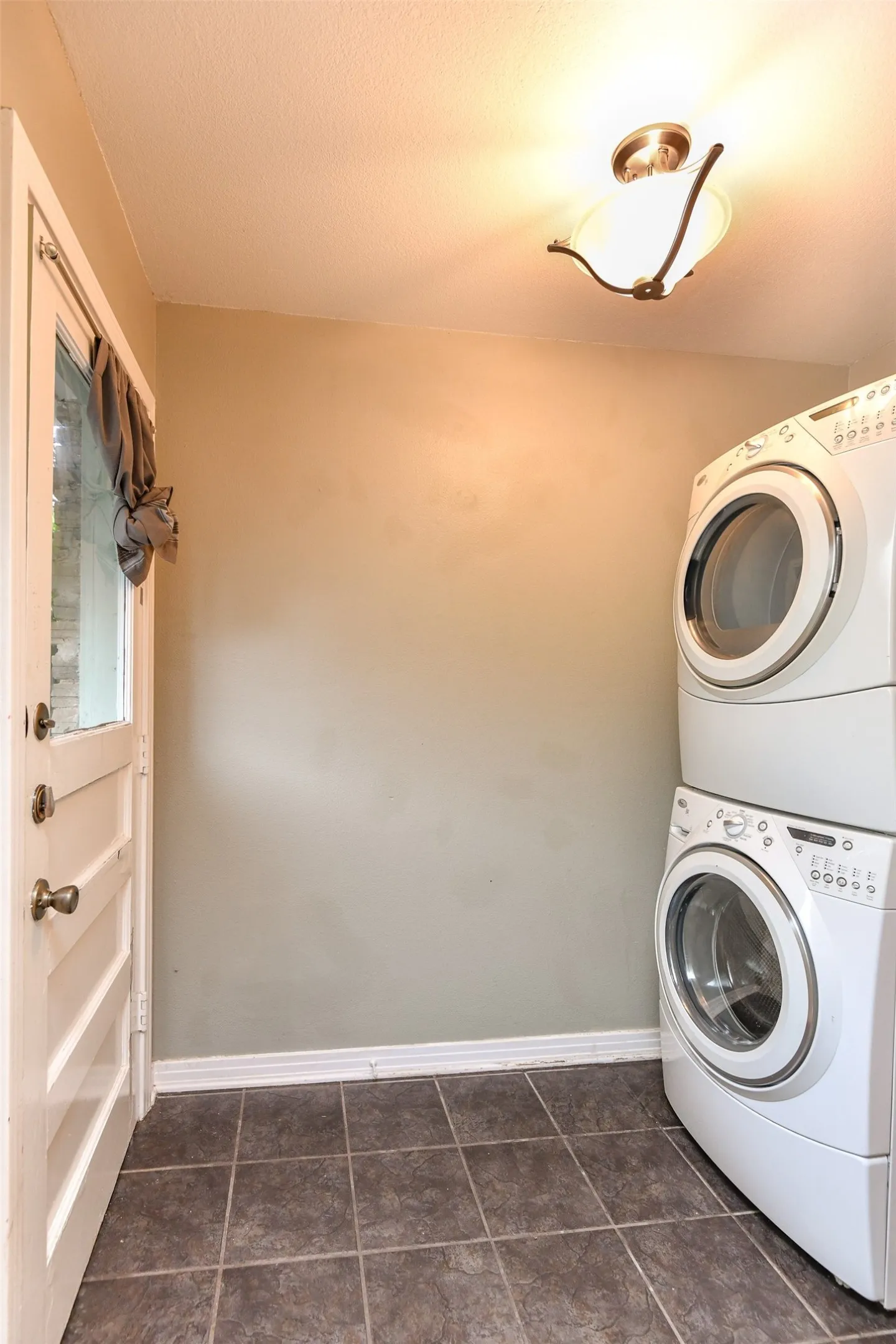 Washroom featuring a textured ceiling, dark tile patterned flooring, and stacked washer and clothes dryer