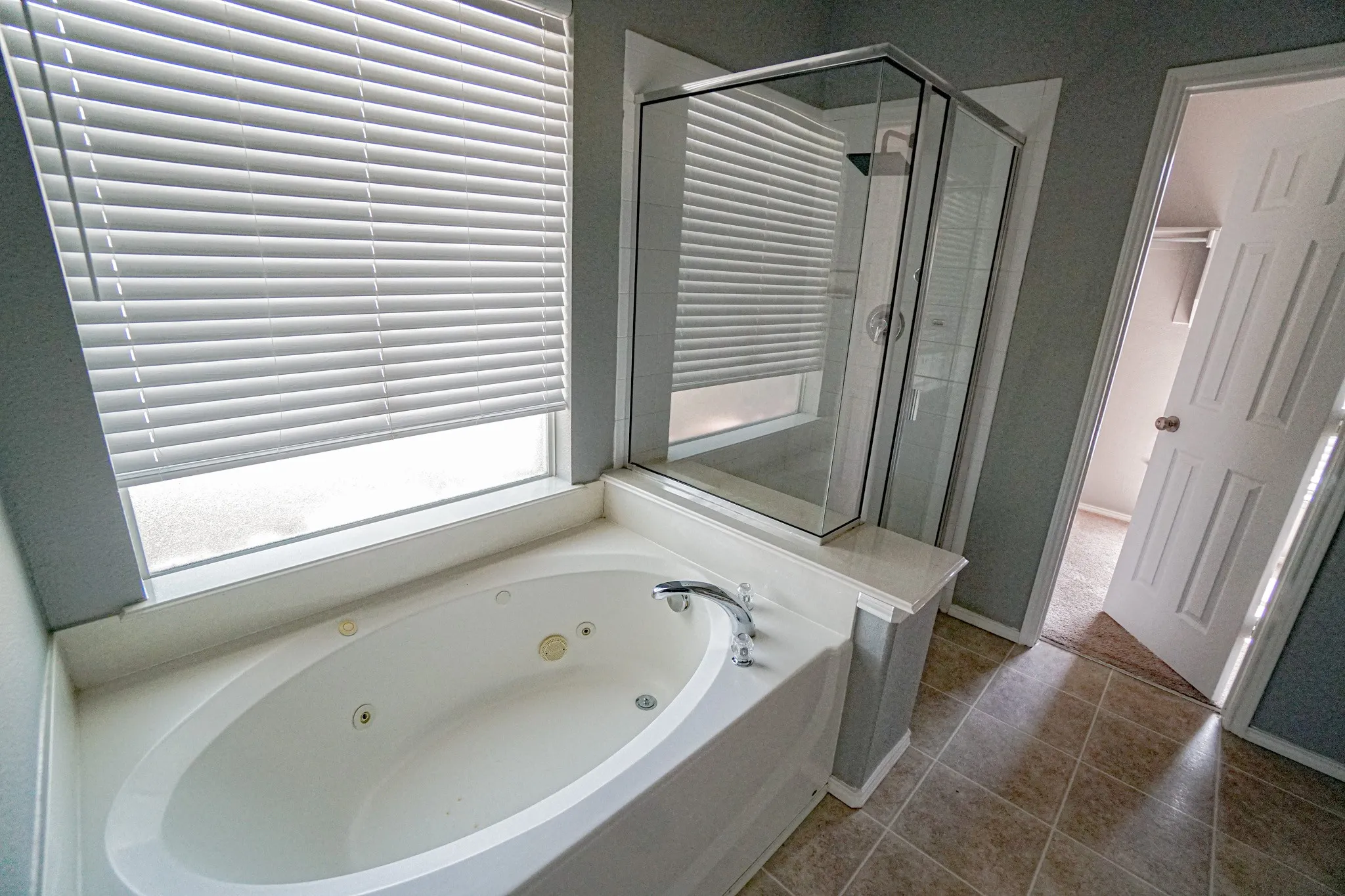 Jetted soaking tub, glass-enclosed shower, window with privacy blinds, and tile flooring