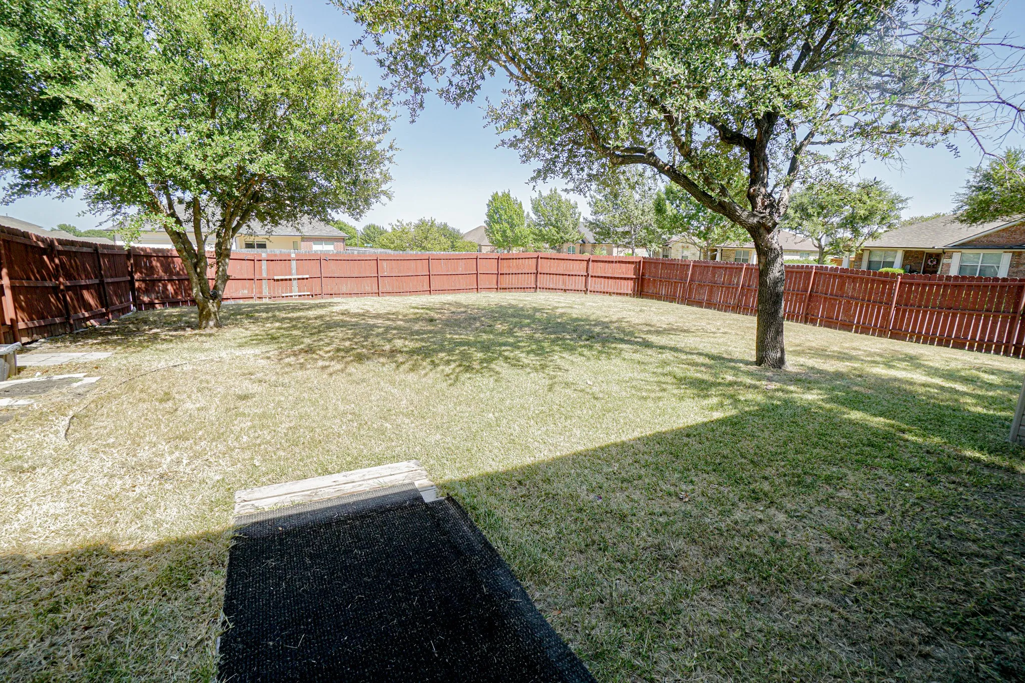 Expansive backyard featuring a wood fence, mature shade trees, and a ground-level patio