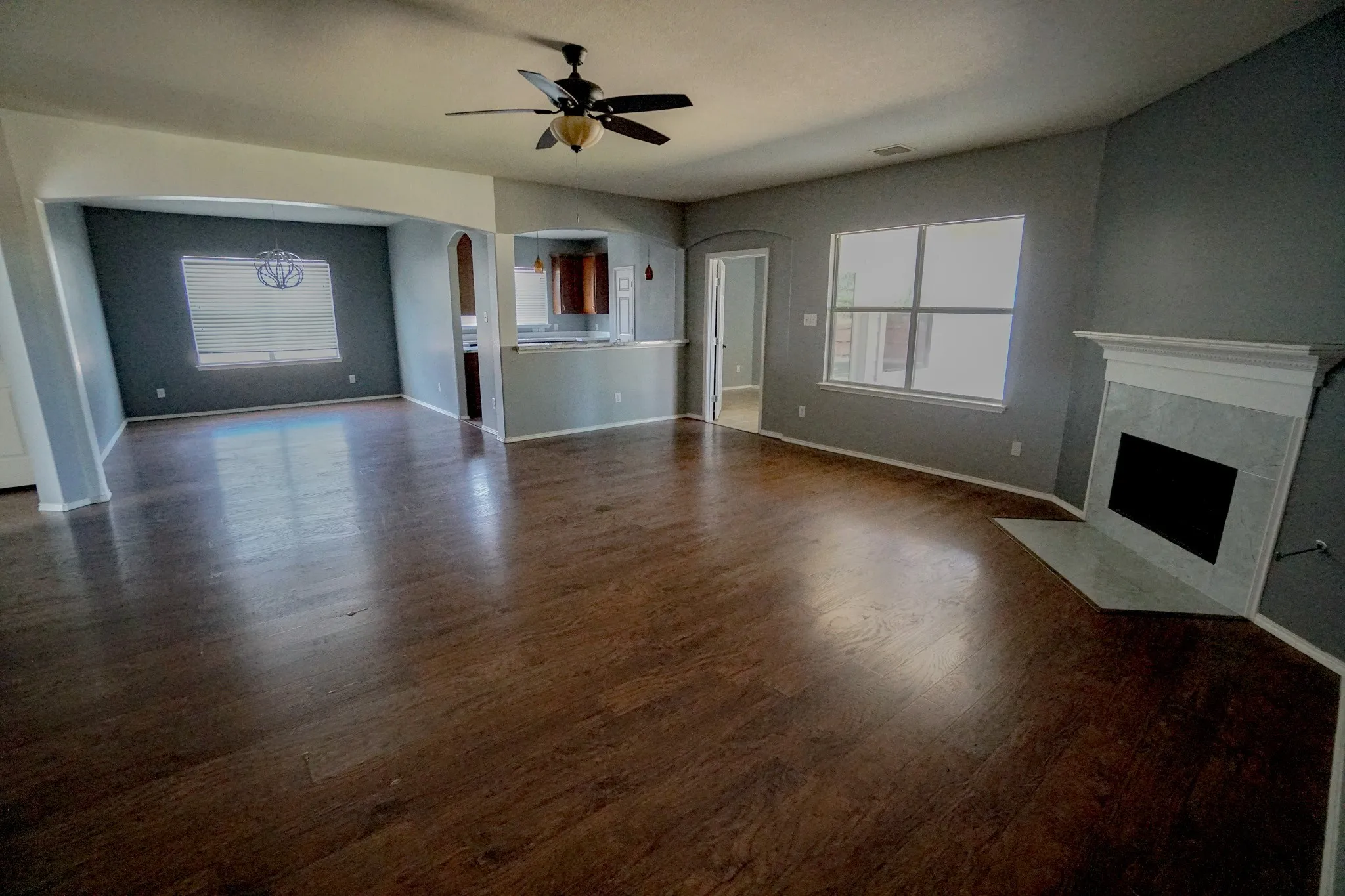 Spacious interior featuring wood-finish flooring, a ceiling fan, a fireplace with a white mantel and tile surround, and multiple windows with blinds