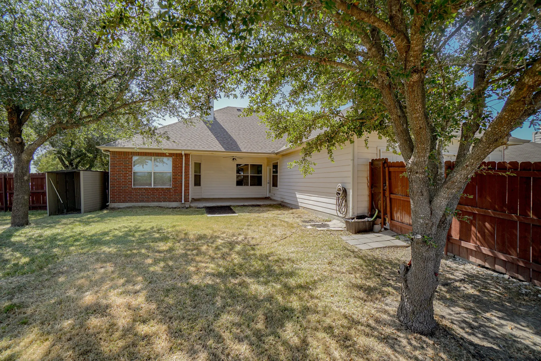 Expansive backyard featuring mature trees, a privacy fence, a covered patio, and a storage shed. 2285 Timber Creek Dr, Rockwall,