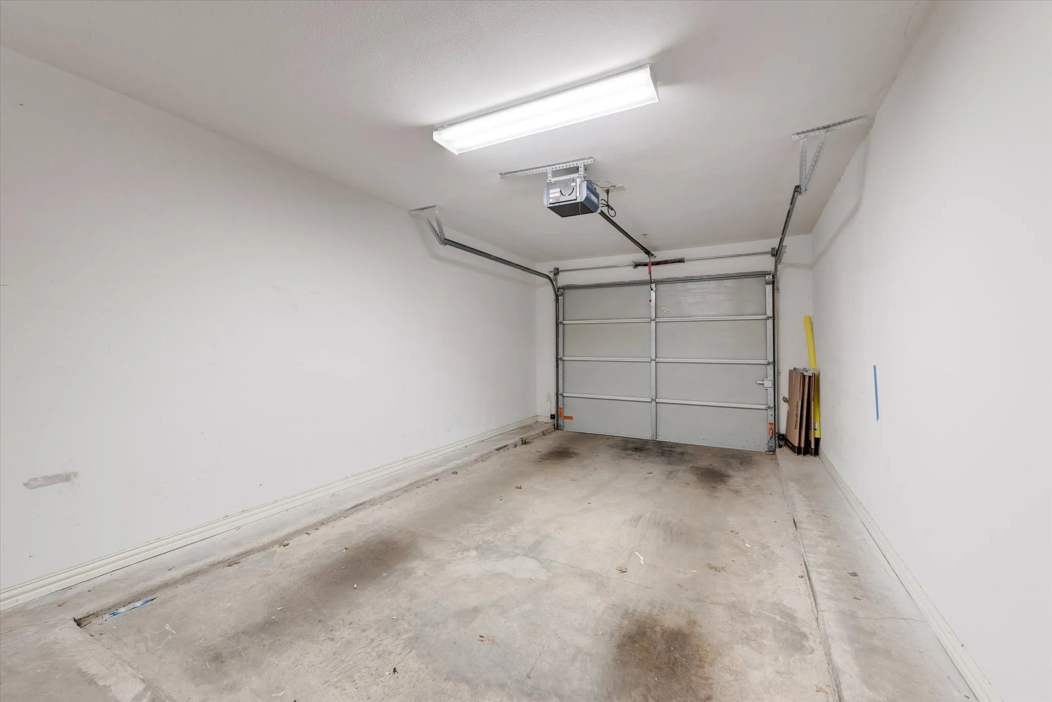Private single-car garage featuring a roll-up door, exposed concrete flooring, and an overhead lighting fixture