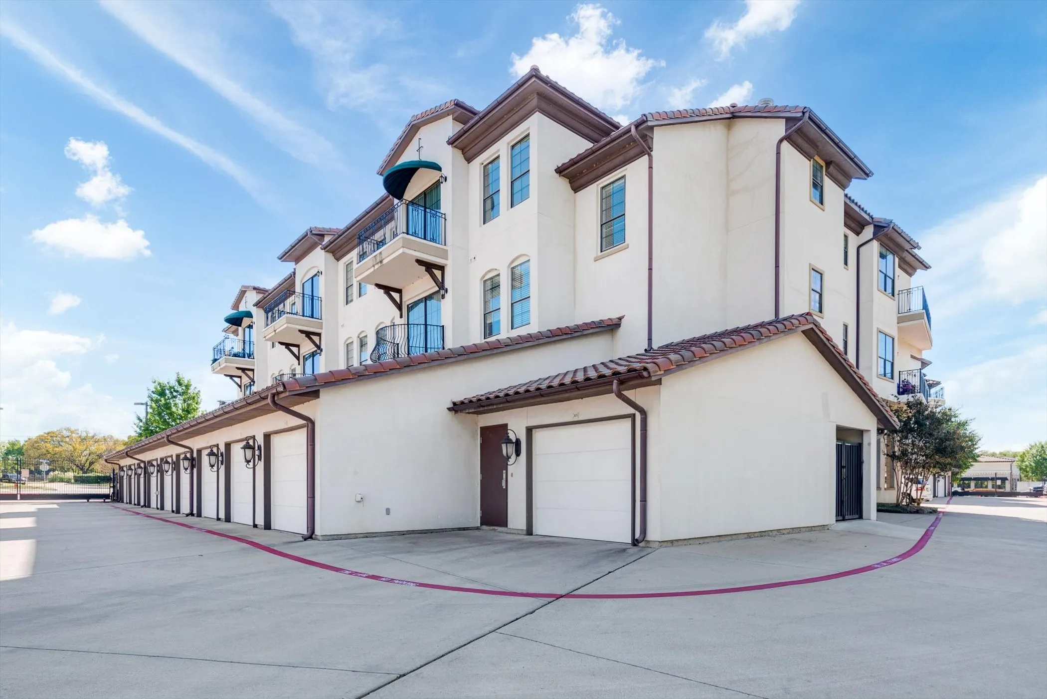 Stucco exterior with tile roofing, individual garage doors, multiple balconies with awnings, and exterior wall sconces