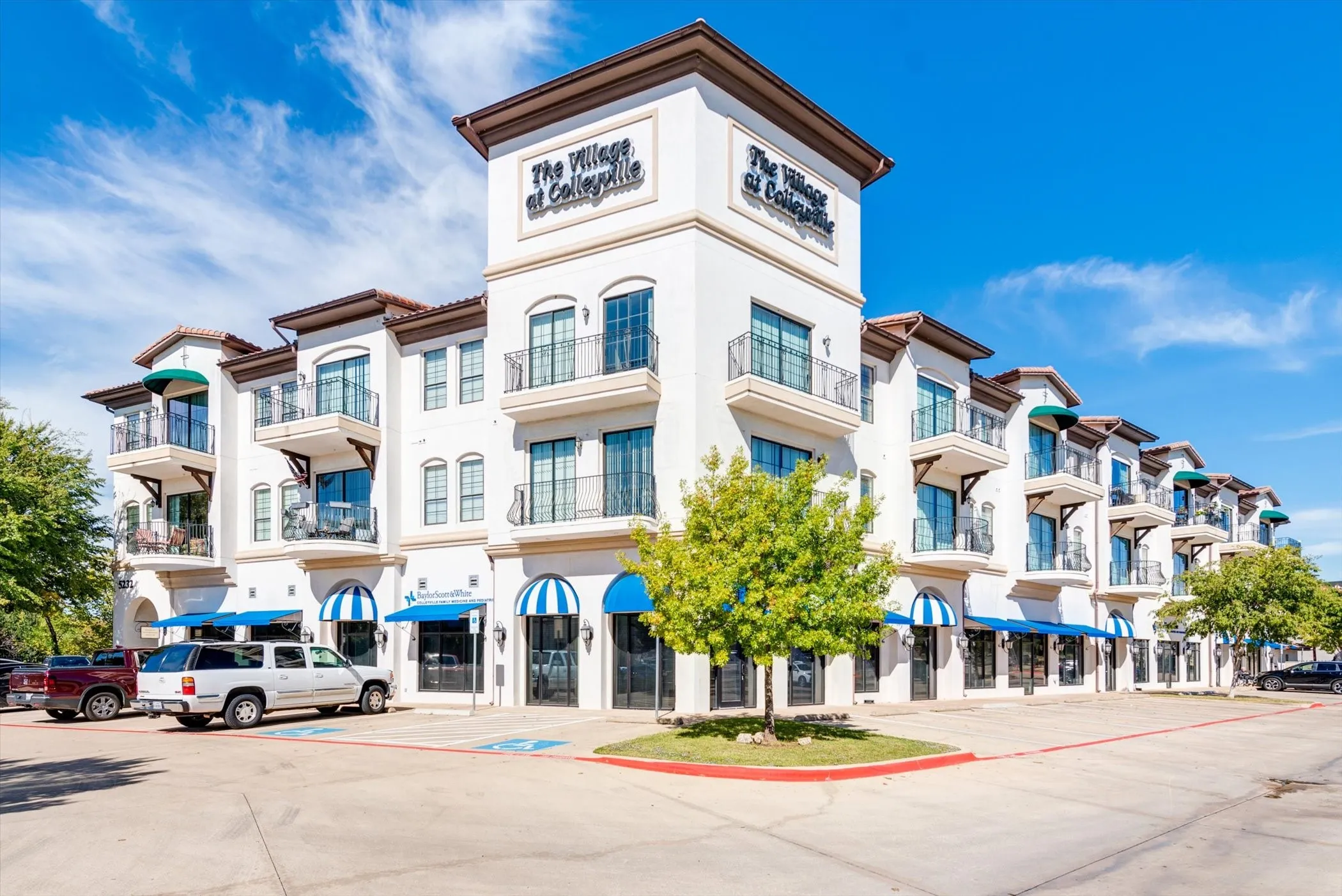 Multi-story building featuring a stucco exterior, arched awnings, Juliet balconies with wrought iron railings, and a prominent tower