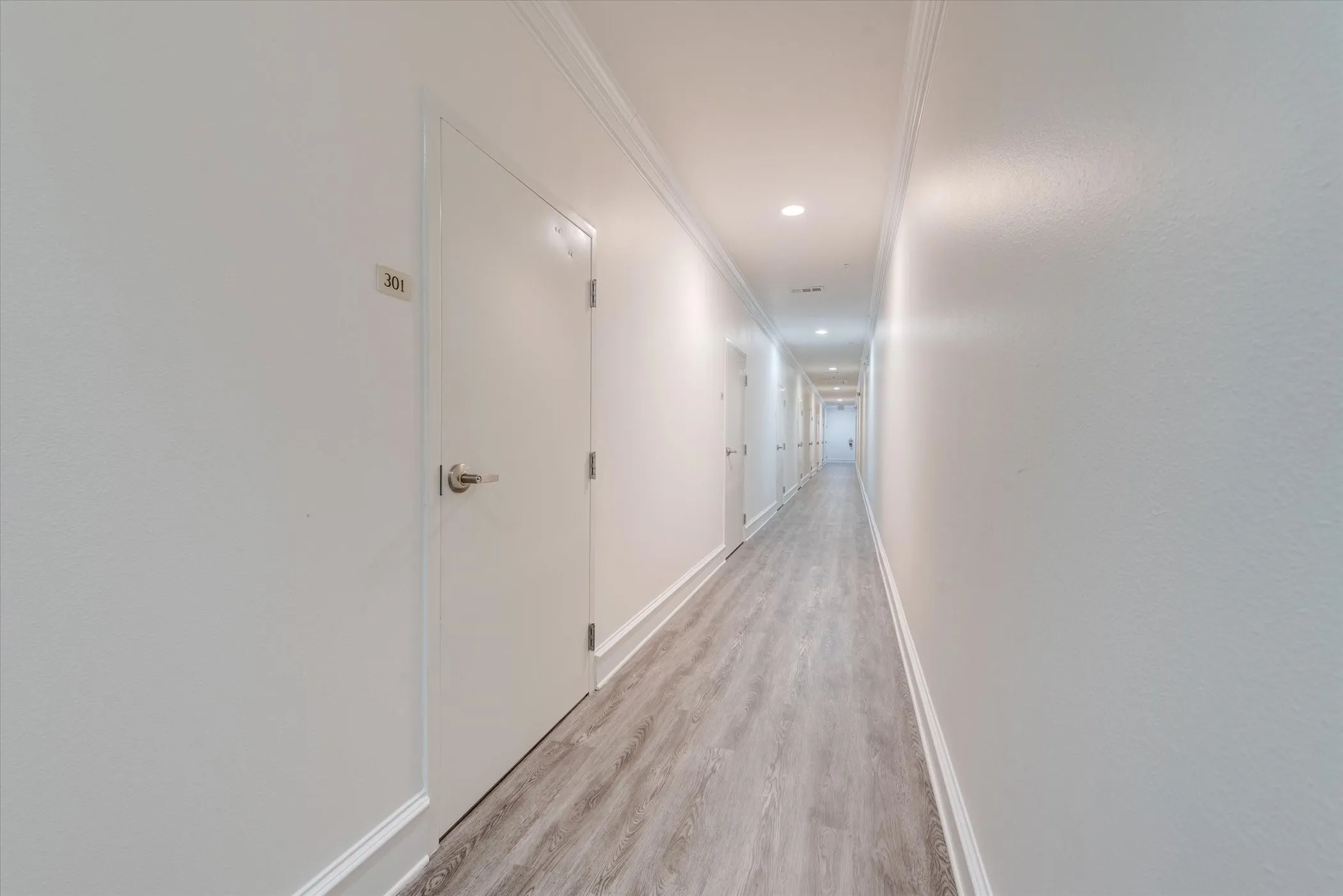 Long hallway to private garages featuring recessed lighting, crown molding, wood-finish flooring, and multiple doors with contemporary hardware