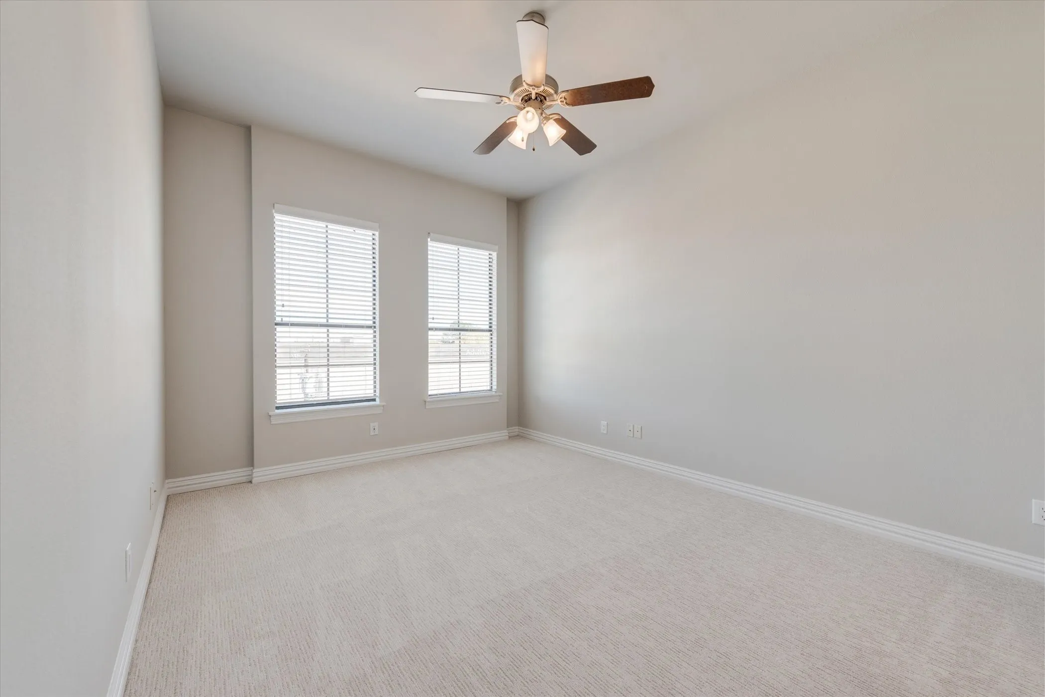 Vaulted ceiling with an attached ceiling fan, dual windows with blinds, and neutral carpeting
