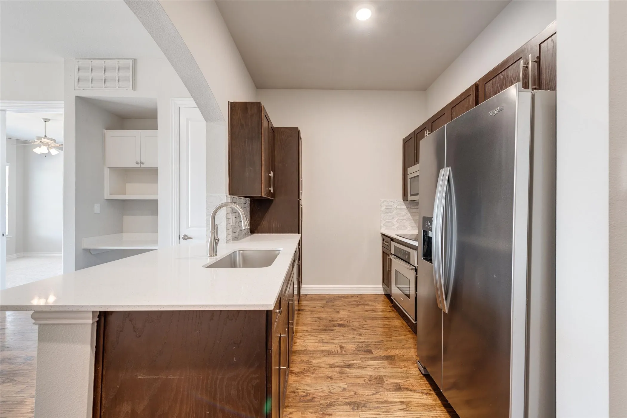 Kitchen featuring wood-finish flooring, dark wood cabinetry, white countertops, stainless steel appliances, and a mosaic tile backsplash