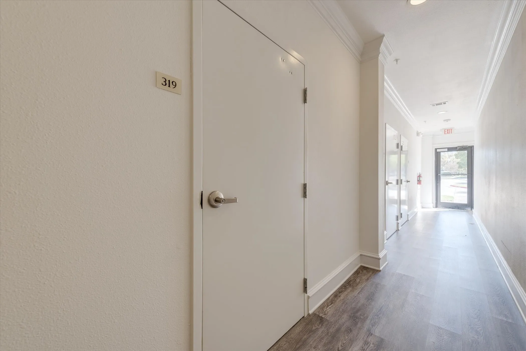 Hallway to private garages and mailboxes, featuring wood-finish flooring, white walls, and crown molding