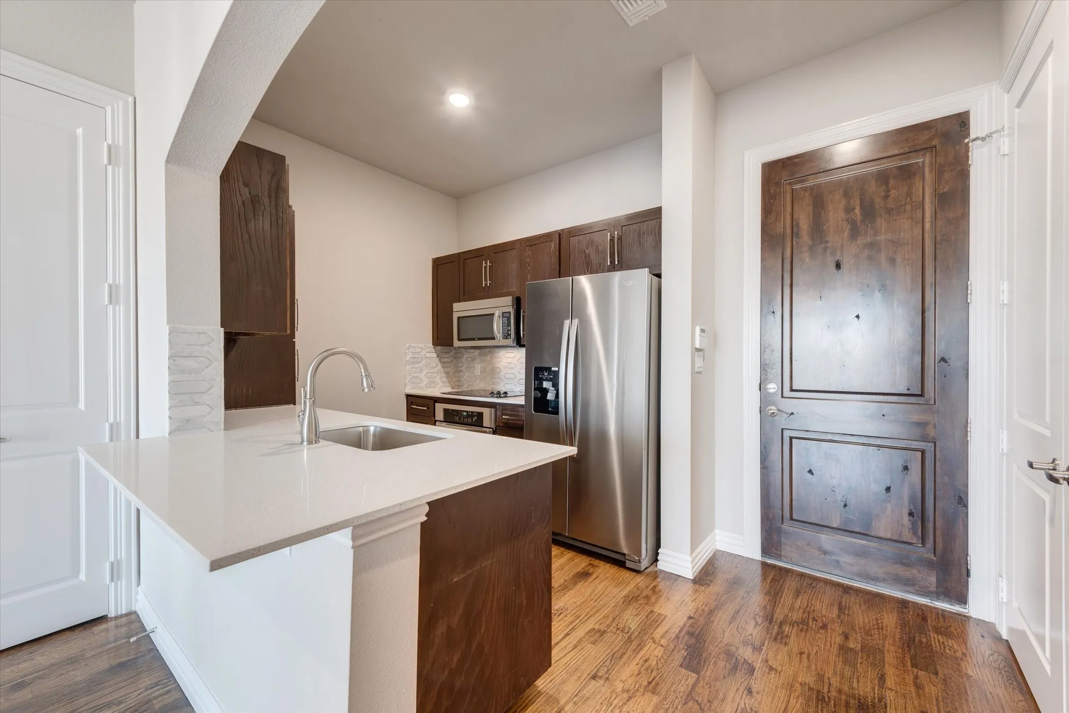 Kitchen featuring a single-basin sink, stainless steel appliances, dark wood-finish cabinetry, and a light-toned countertop
