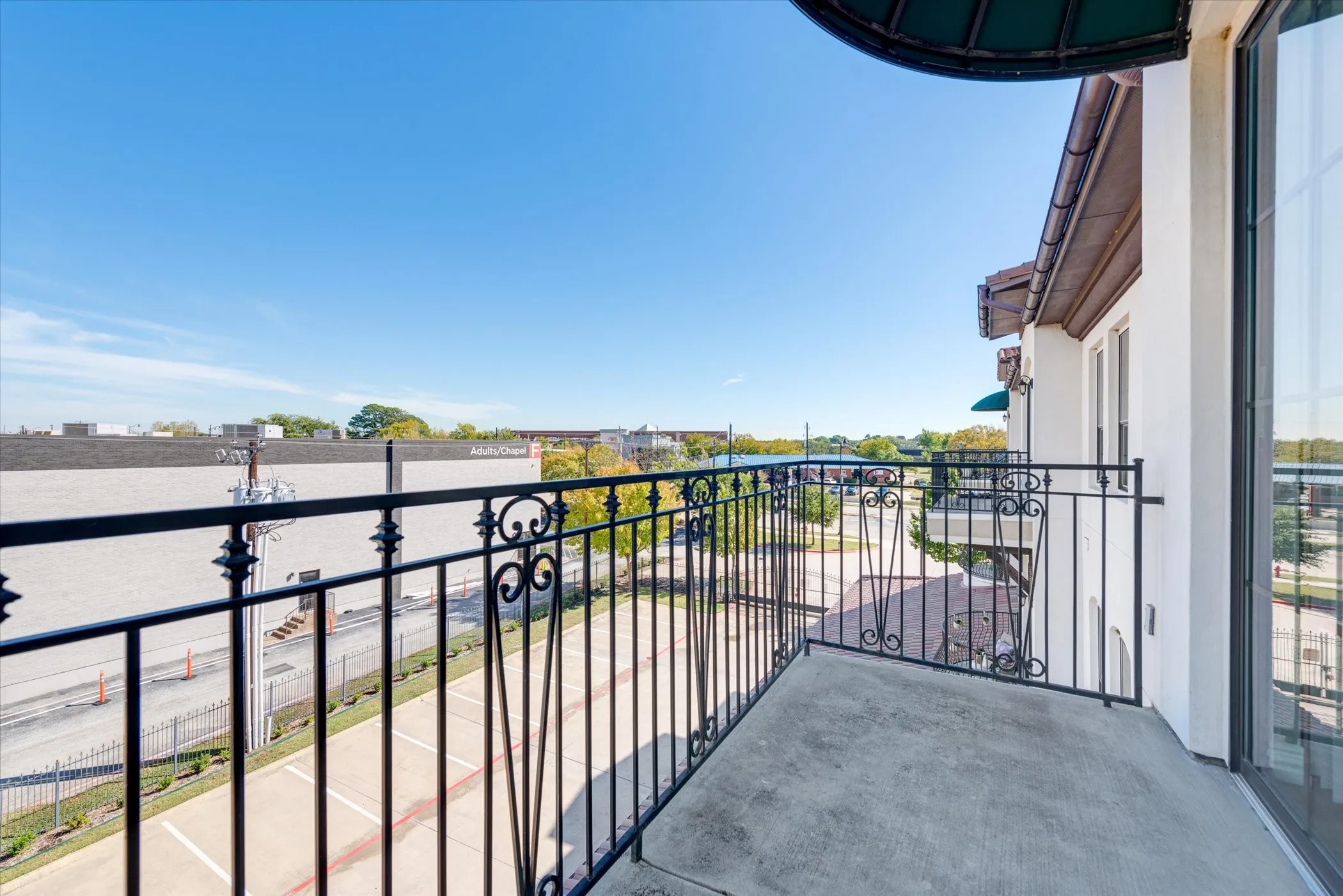 Private balcony featuring ornate wrought iron railings, a concrete surface, and a wall-mounted awning