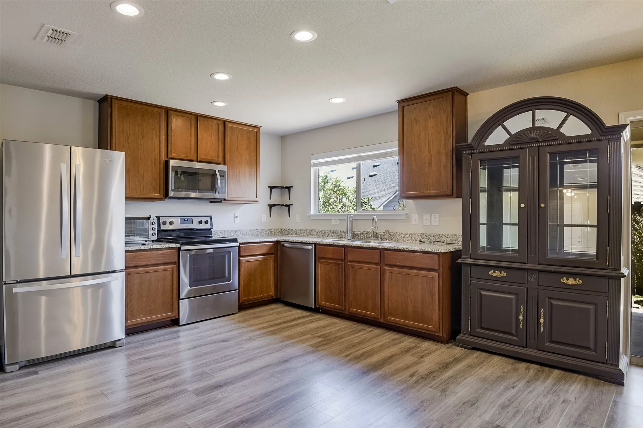 Kitchen featuring wood-finish flooring, recessed lighting, wood cabinetry, stainless steel appliances, and stone countertops