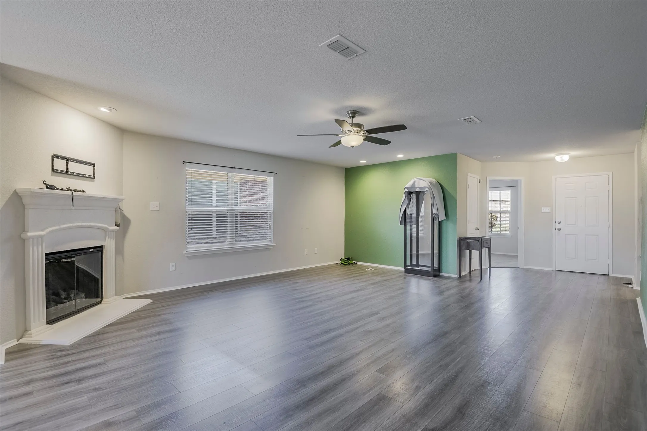 Wood-finish flooring, recessed lighting, ceiling fan with integrated light fixture, interior fireplace with decorative mantel, and a window with blinds