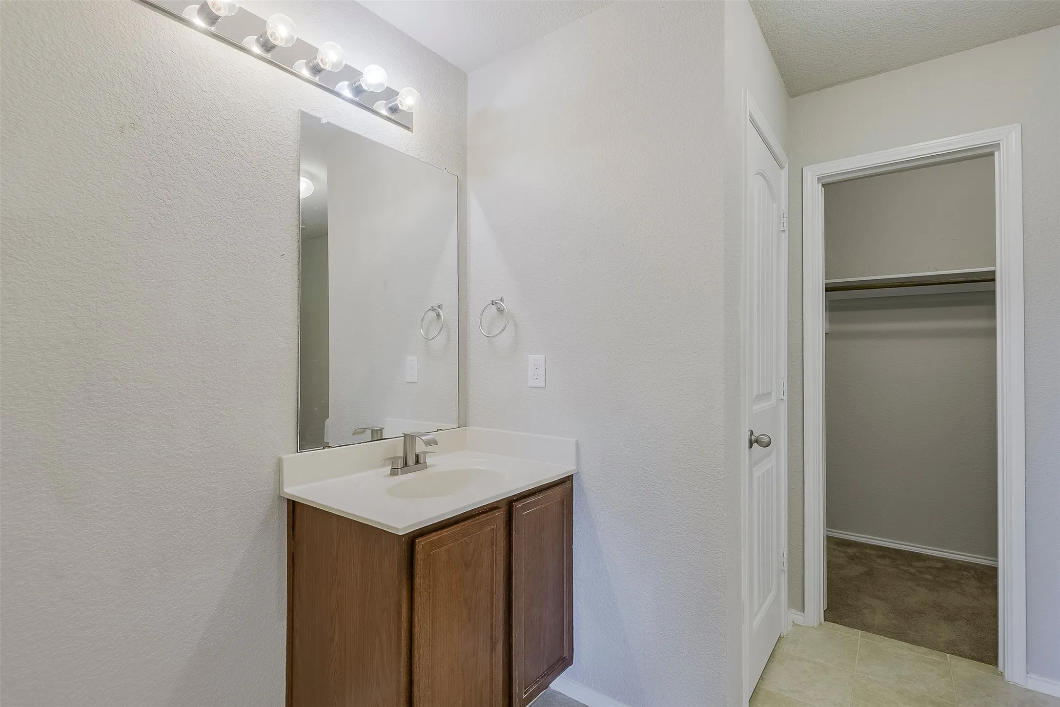Vanity with wood-finish cabinetry, integrated sink, and white countertop