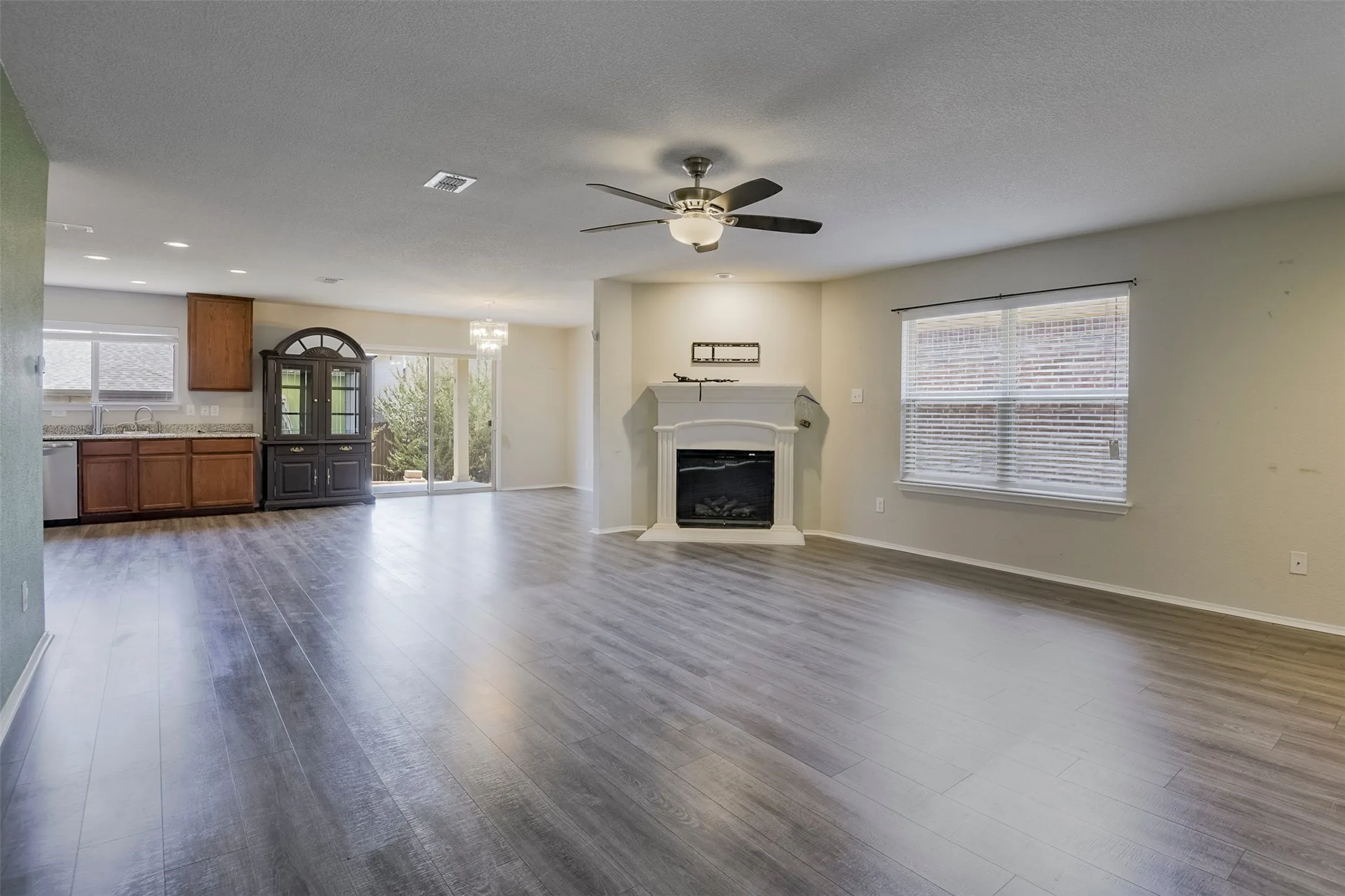 Spacious living area featuring wood-finish flooring, a fireplace with a mantel, and a ceiling fan