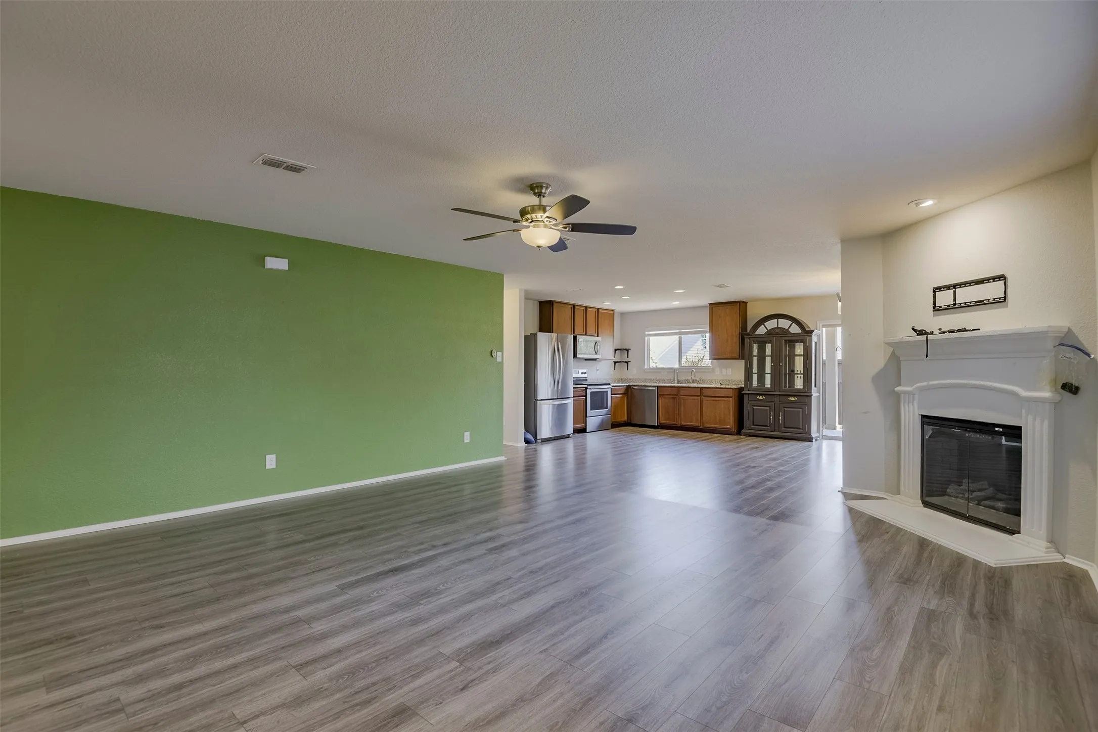 Spacious room featuring wood-finish flooring, a ceiling fan, and a fireplace with a white mantel