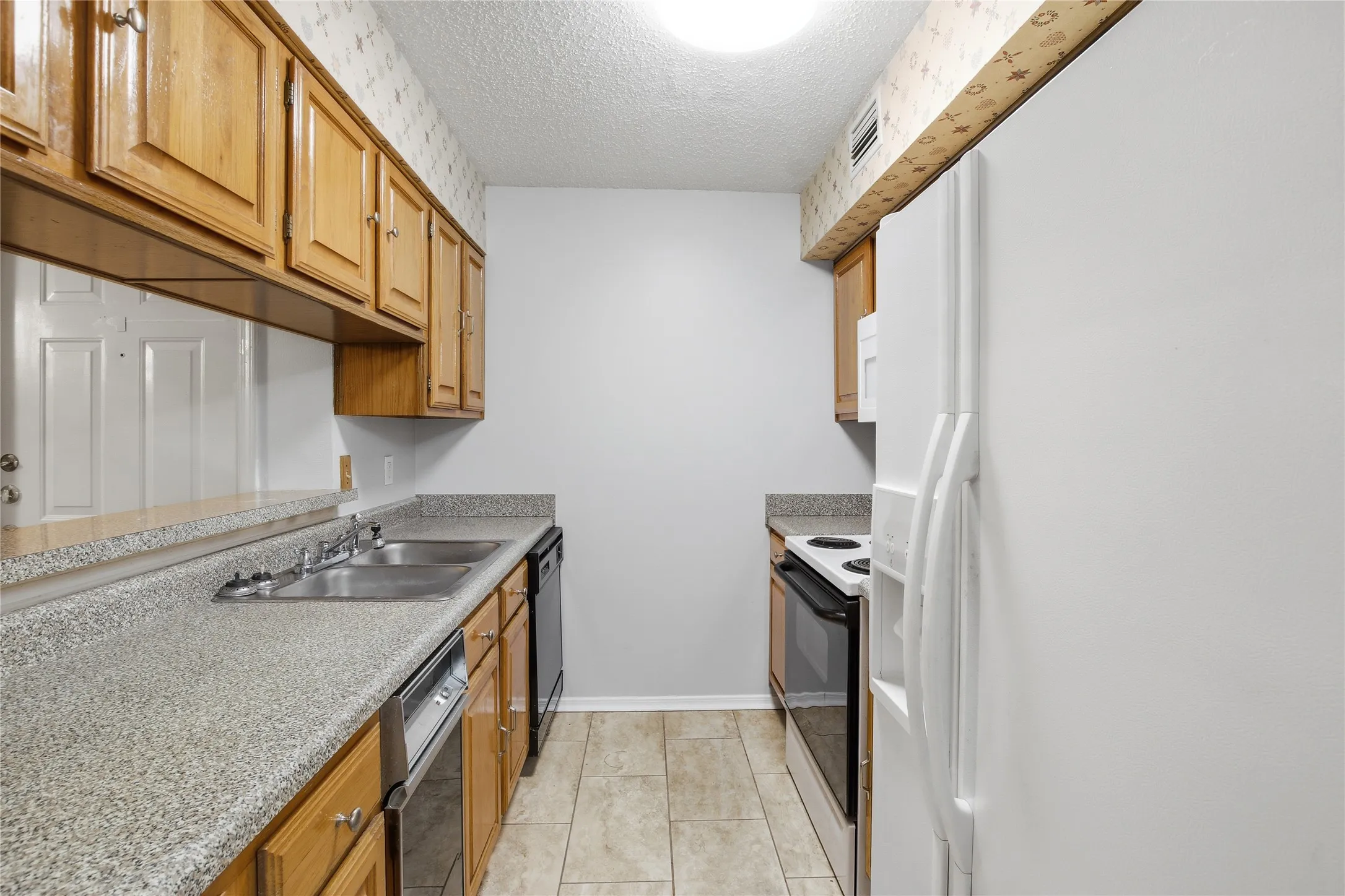 Wood-finish cabinetry, light-colored speckled countertops, a stainless steel sink, tiled flooring, and a white oven