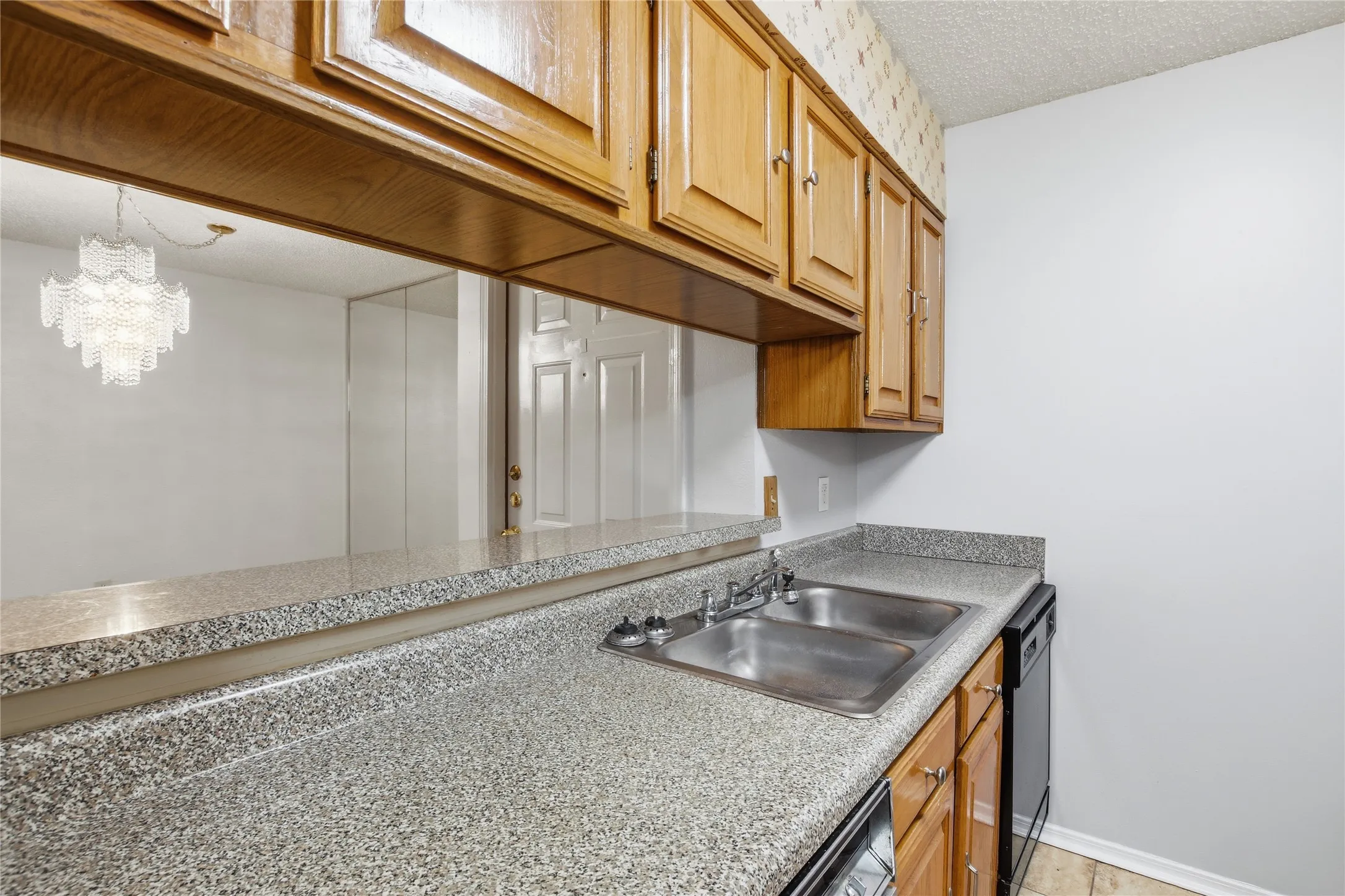 Kitchen featuring light wood-finish cabinetry, speckled countertops, and a double basin stainless steel sink