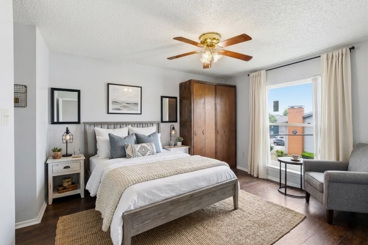 Wood-finish flooring, ceiling fan with light fixture, large window with natural light, and built-in wood-paneled wardrobe