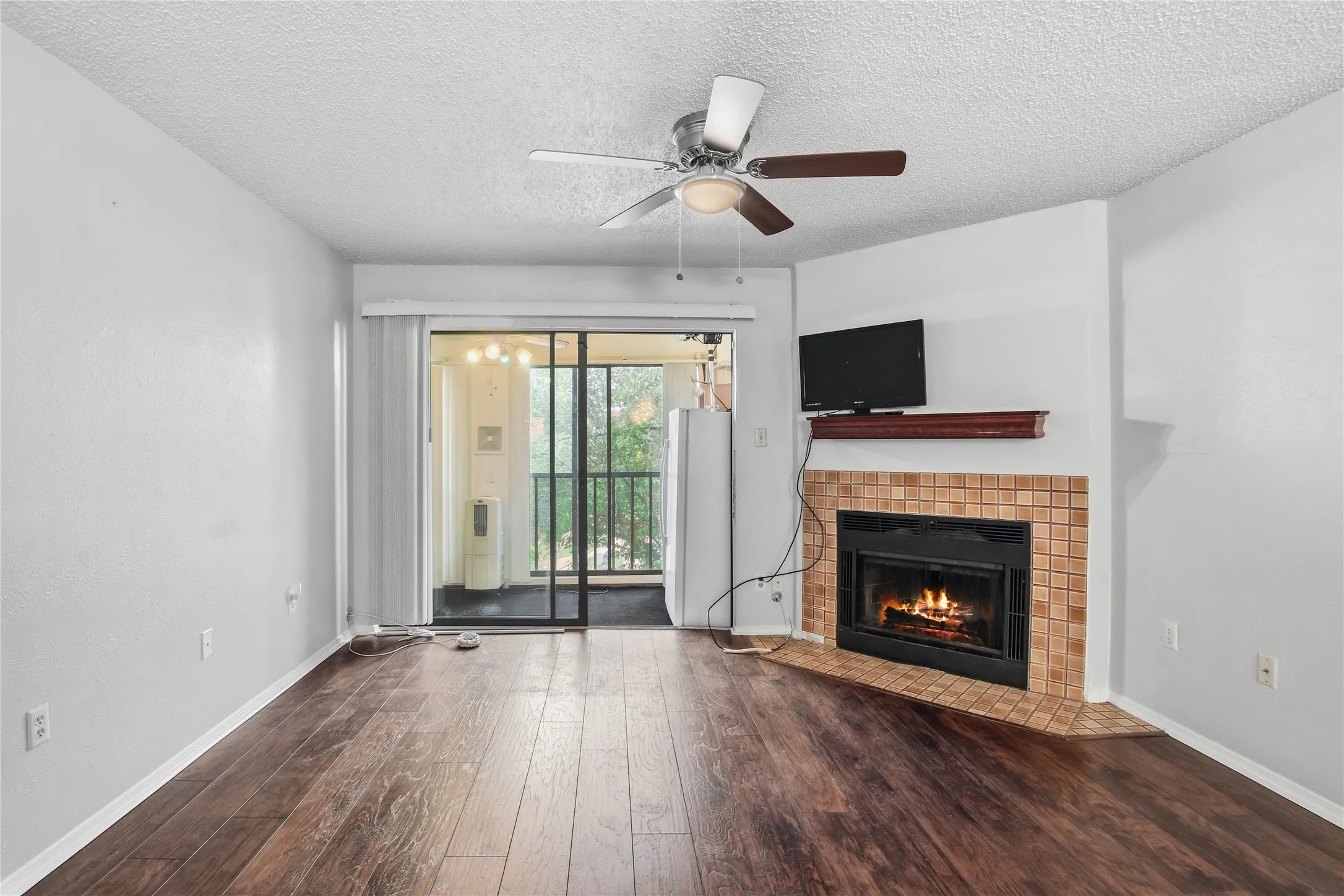 Wood-finish flooring, built-in fireplace with tile surround, ceiling fan with integrated lighting, and glass sliding door access to an enclosed porch