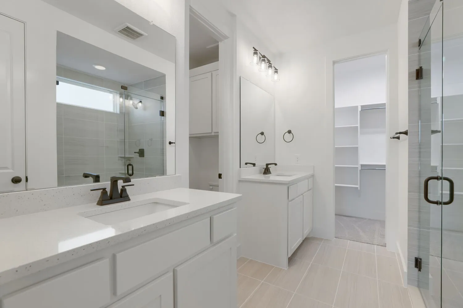 Dual vanity with white cabinetry and integrated sinks, glass-enclosed shower with tile surround, and an adjacent walk-in closet with built-in shelving