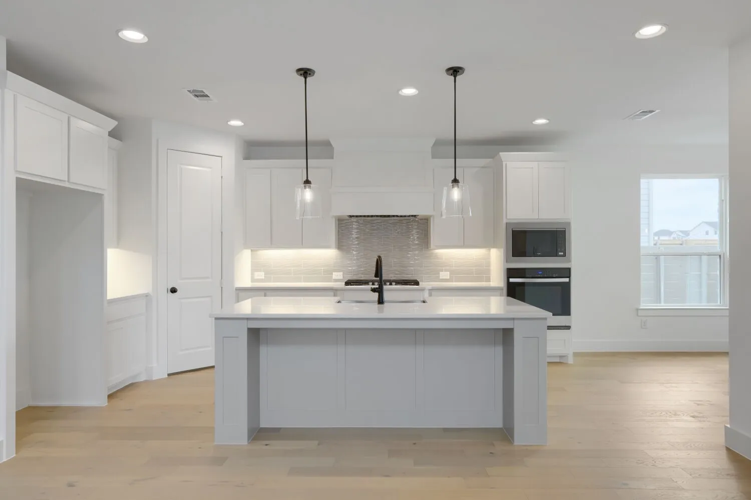 Kitchen featuring light wood-finish flooring, white cabinetry, a built-in oven and microwave, and a central island with dual pendant lighting