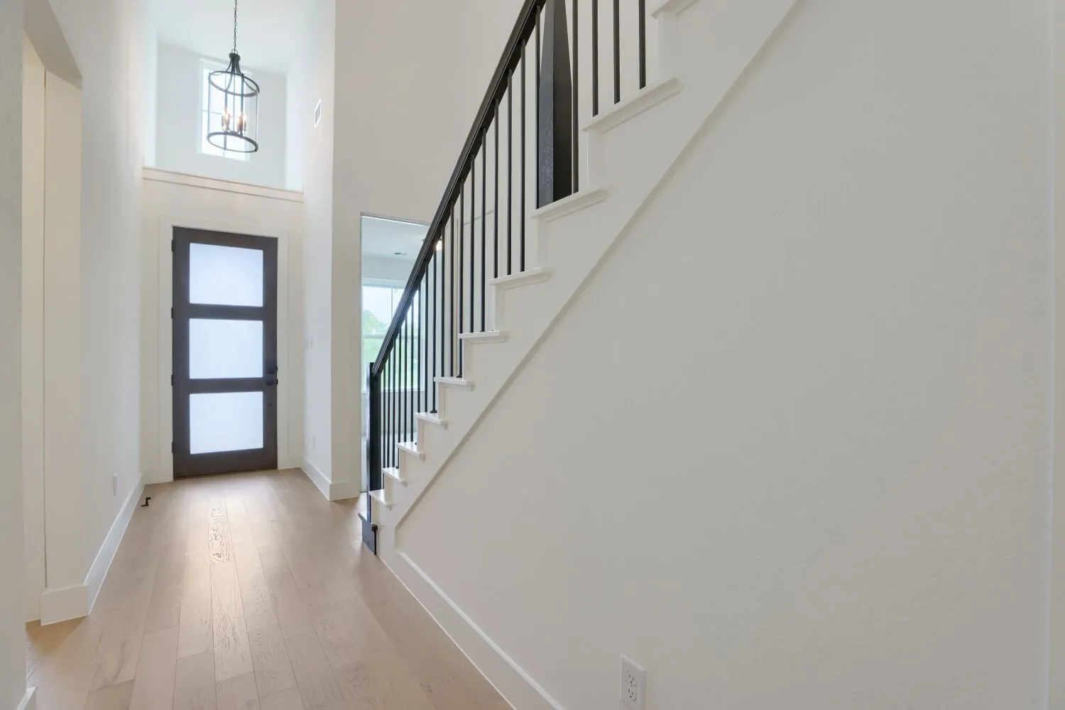 Two-story entryway featuring a modern front door with frosted glass panels, wood-finish flooring, a contemporary staircase with dark balusters, and a decorative pendant light fixture
