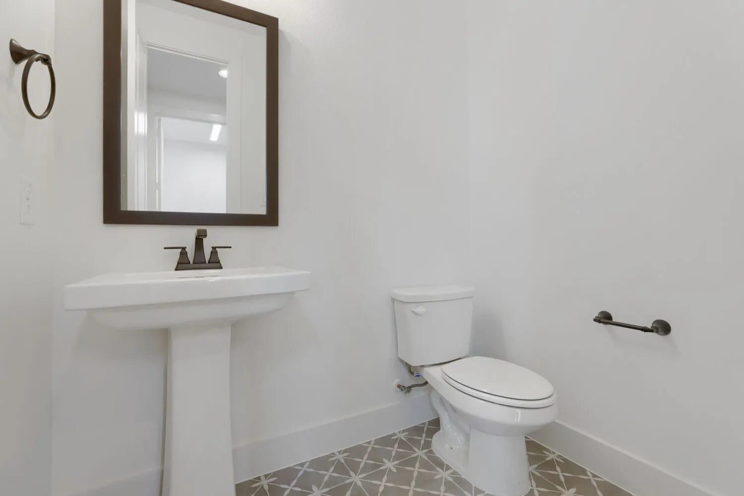 Pedestal sink with dark bronze fixtures, framed mirror, and patterned floor tile