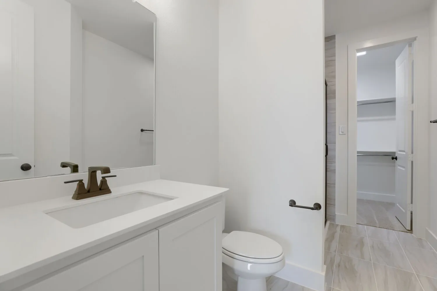 White vanity with an integrated sink, bronze-finish faucet, and a large wall mirror