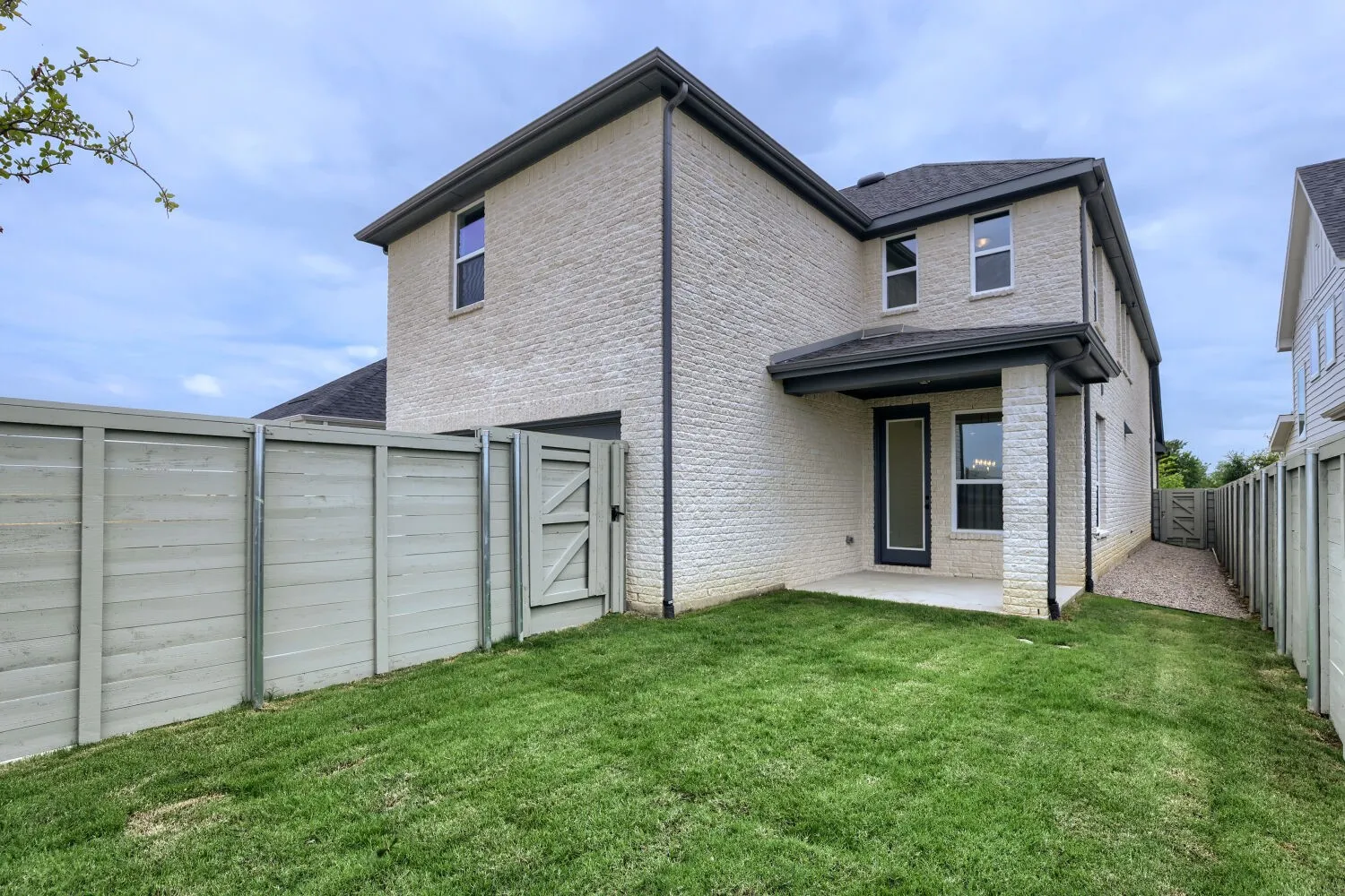 Brick exterior with dark gutters, covered patio, private fenced yard, and a side access gate