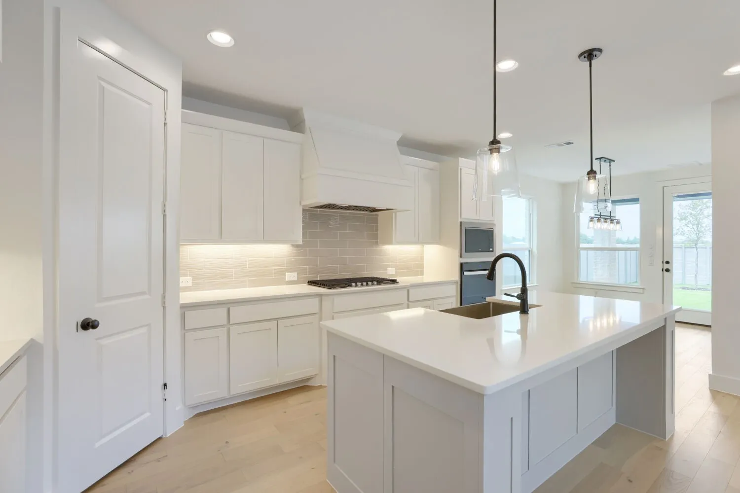 Kitchen featuring a large central island with solid surface countertop, white cabinetry, integrated stainless steel appliances, and light wood-finish flooring
