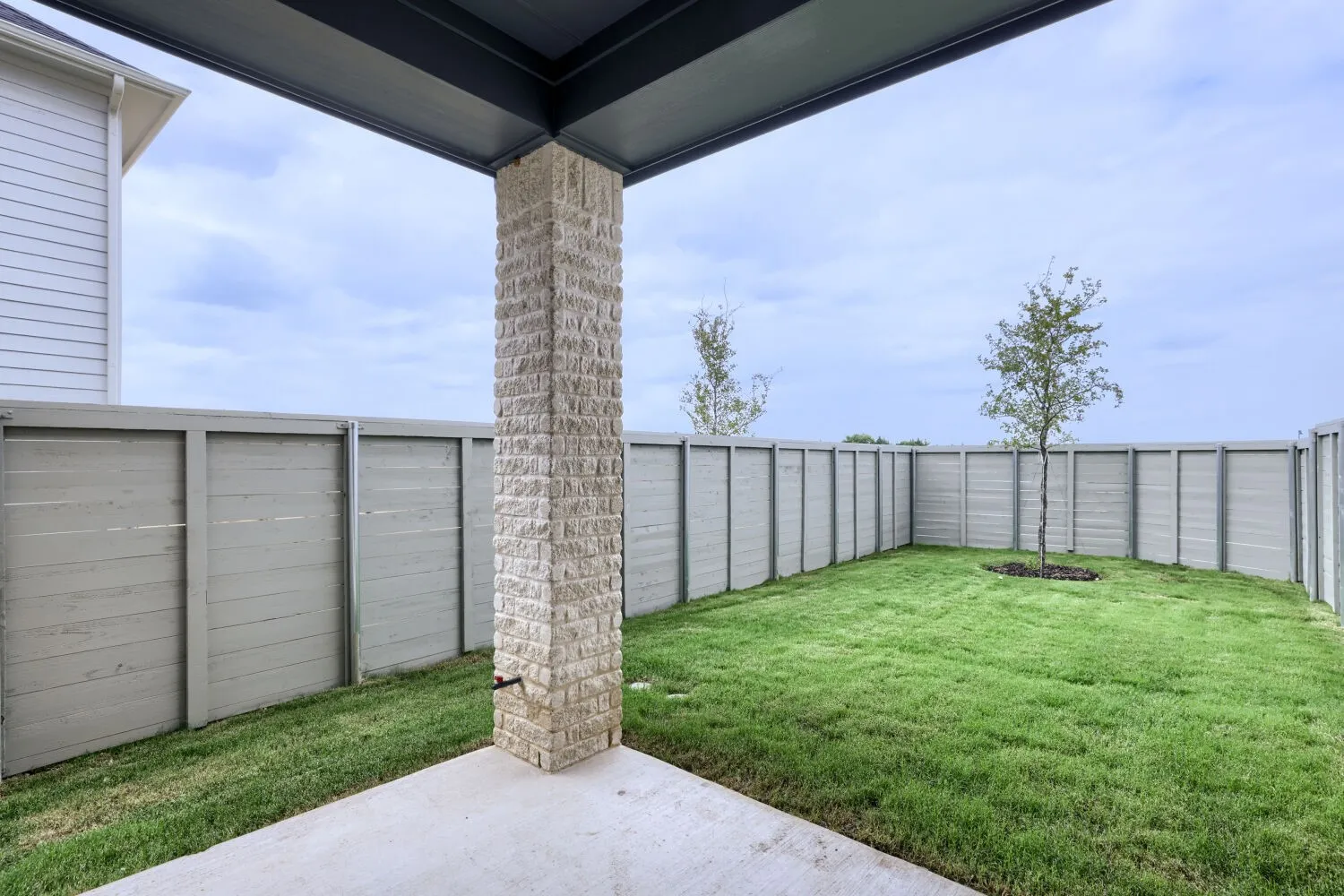 Covered patio with a stone-finish pillar, concrete flooring, and an expansive lawn