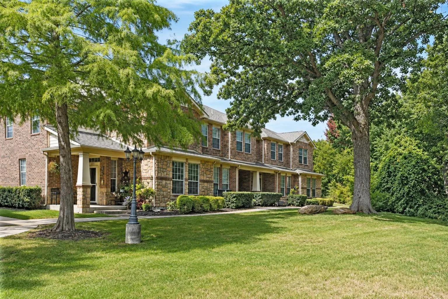 Brick and stone veneer exterior with covered front porches, mature trees, and a spacious lawn