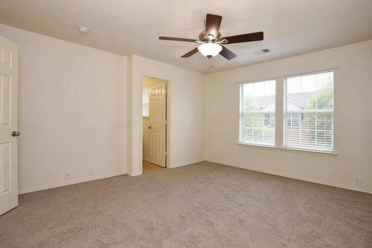 Wall-to-wall carpeting, two panel doors, two windows with blinds, and a ceiling fan with integrated lighting