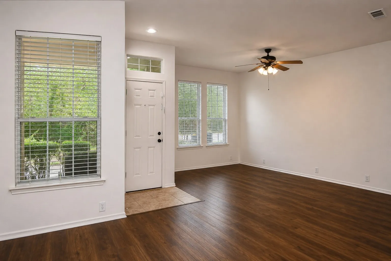 Wood-finish flooring, white walls, multiple windows with blinds, a ceiling fan with integrated lighting, and recessed lighting