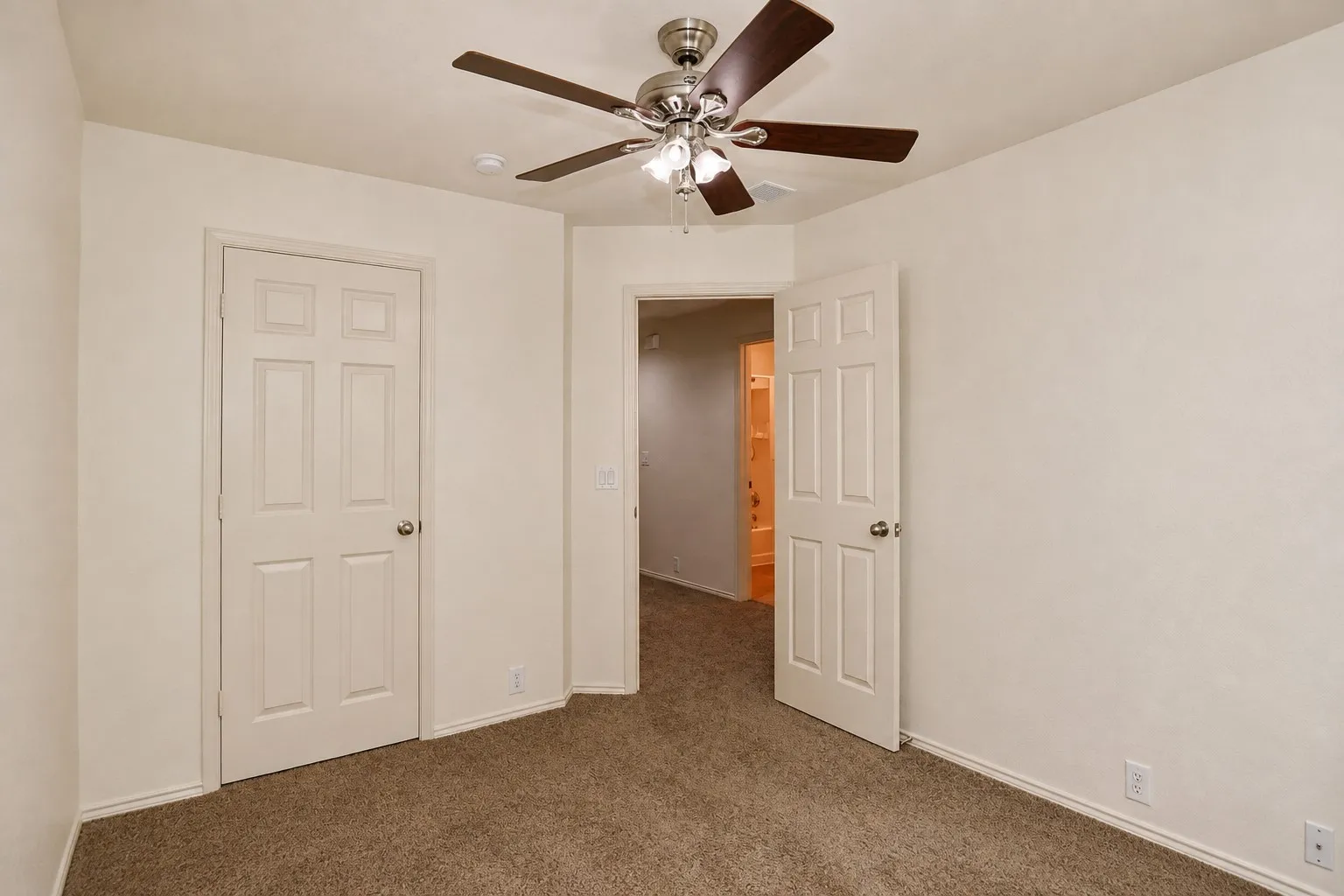 Neutral wall paint, brown carpet flooring, six-panel interior doors, and a ceiling fan with light fixture