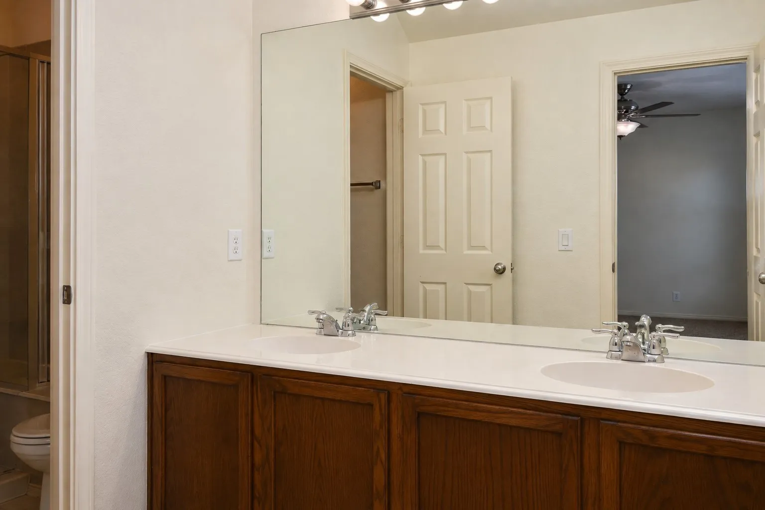 Dual vanity with integrated sinks, chrome fixtures, a full-width mirror, and wood-finish cabinetry