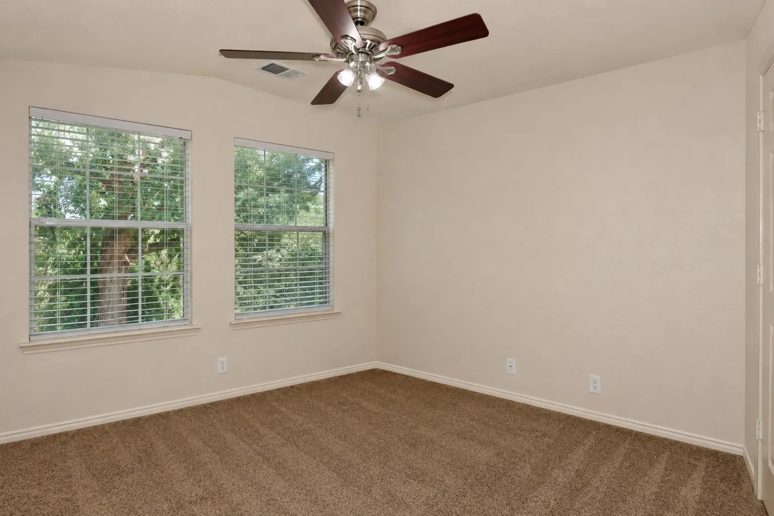 Vaulted ceiling featuring a ceiling fan, dual windows with blinds, carpet flooring, and neutral wall paint