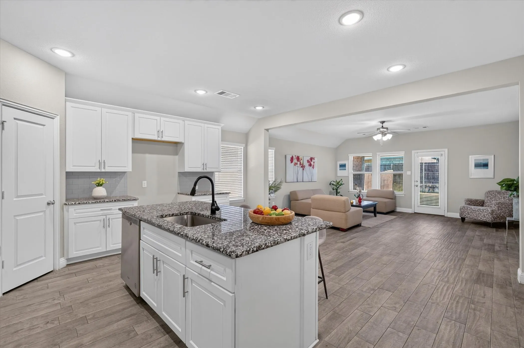 Open-concept living space with wood-finish flooring, recessed lighting, and white cabinetry