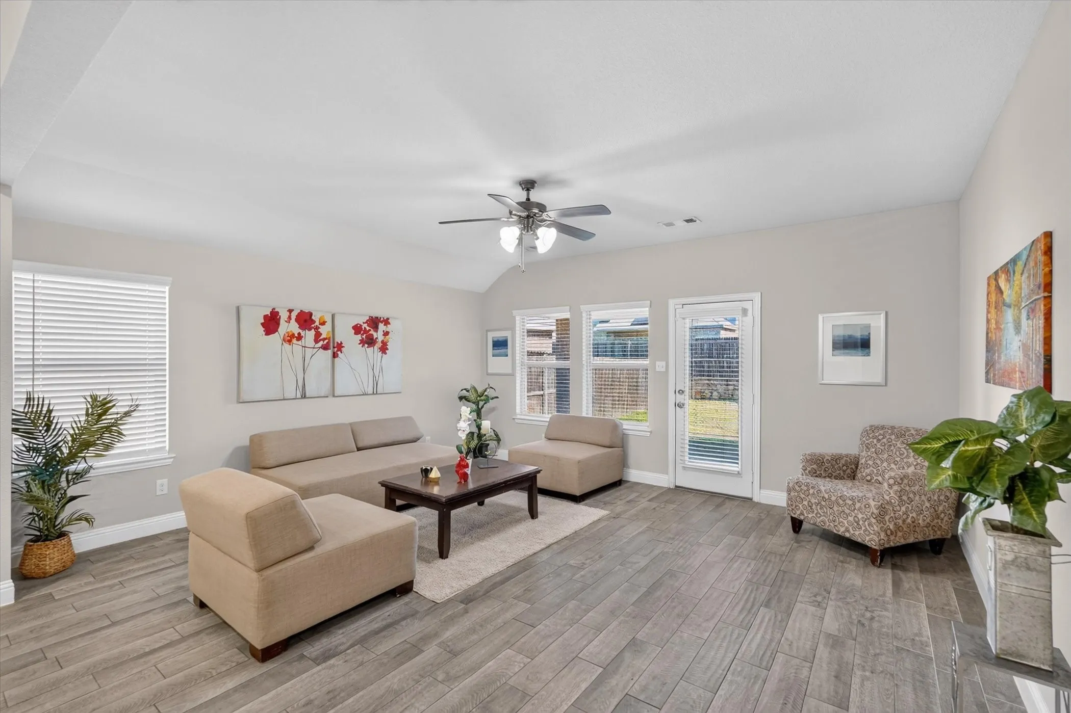 Vaulted ceiling, wood-finish flooring, ceiling fan with light fixture, multiple windows with blinds, and a glass-paneled exterior door