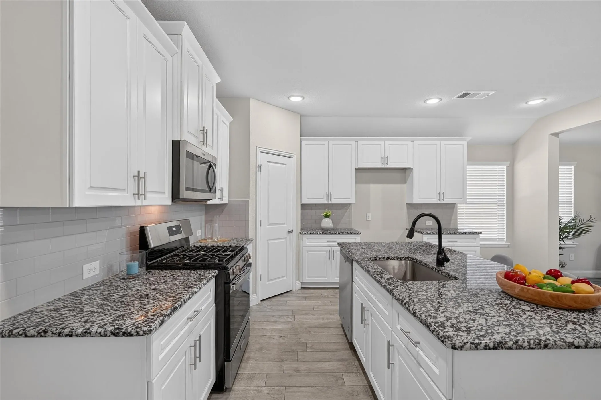 Kitchen featuring white cabinetry, granite countertops, tile backsplash, wood-finish flooring, and a center island with an undermount sink and matte black faucet