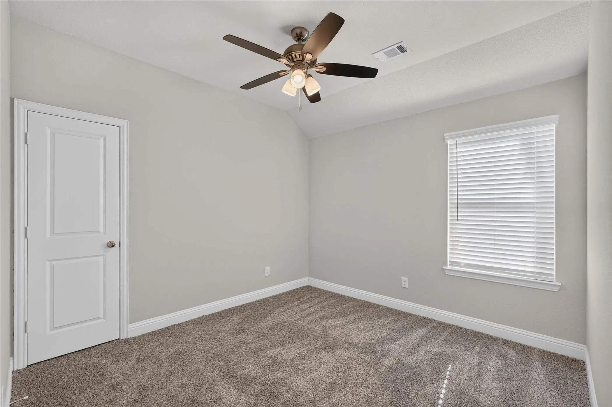 Bright bedroom with neutral wall finishes, plush carpeting, ceiling fan with integrated lighting, and large window with plantation shutters providing natural light and privacy