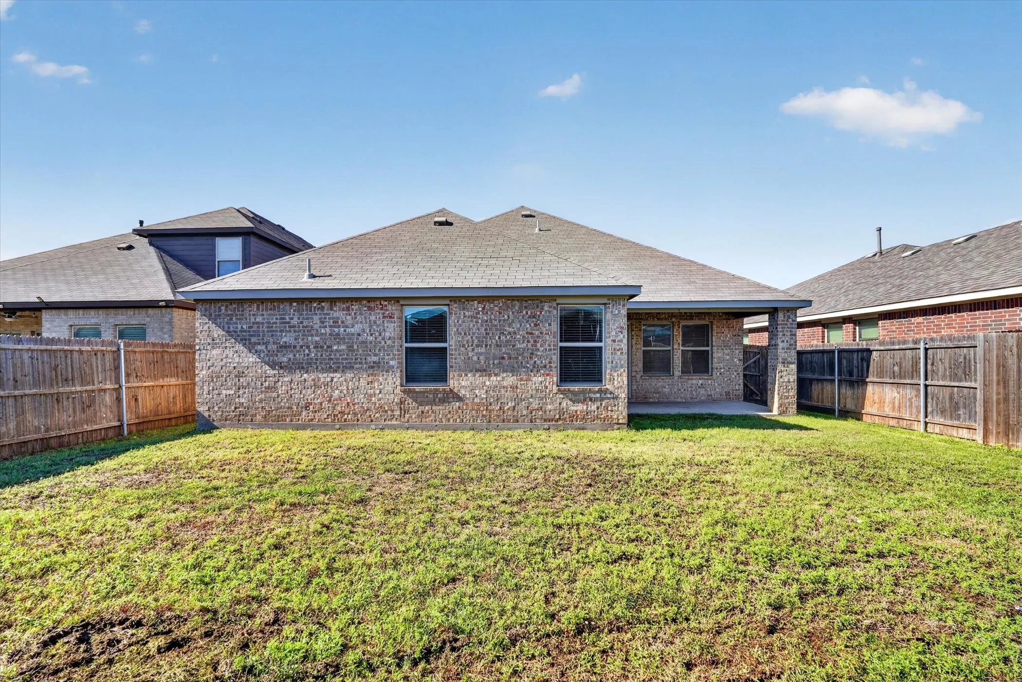 Brick exterior with a covered patio, fenced yard, and a shingle roof