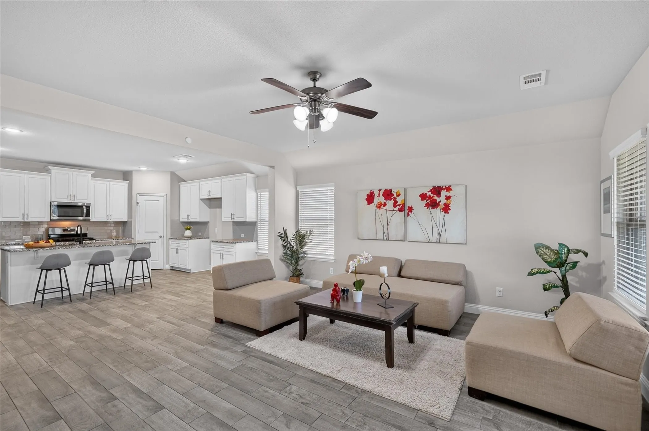 Integrated kitchen and living area with wood-finish flooring, white cabinetry, a built-in kitchen island, and stainless steel appliances