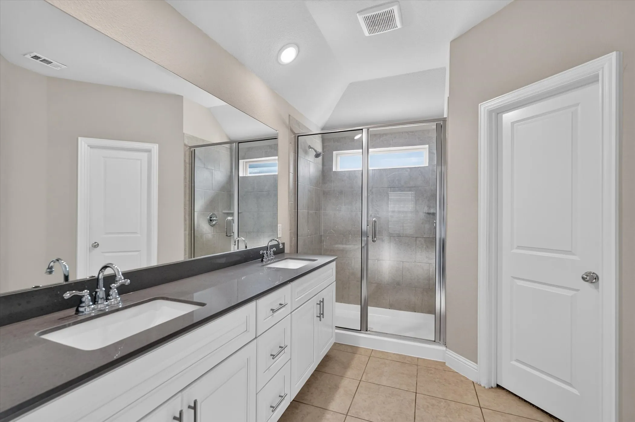Spa-inspired primary bathroom featuring a double vanity with dark countertops, white cabinetry, and polished nickel fixtures