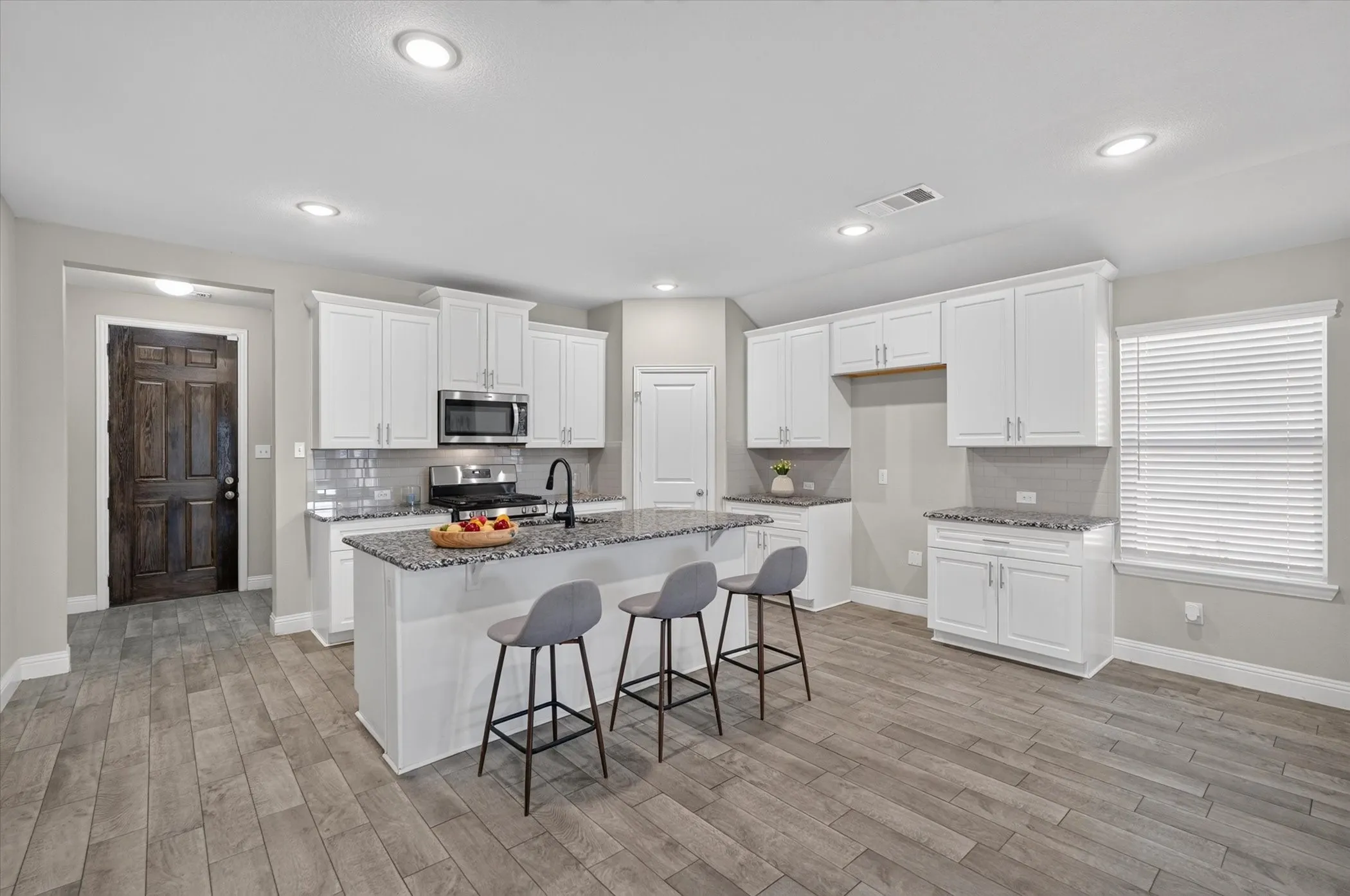 Open-concept kitchen featuring an island with a granite countertop, stainless steel appliances, a tile backsplash, and white cabinetry