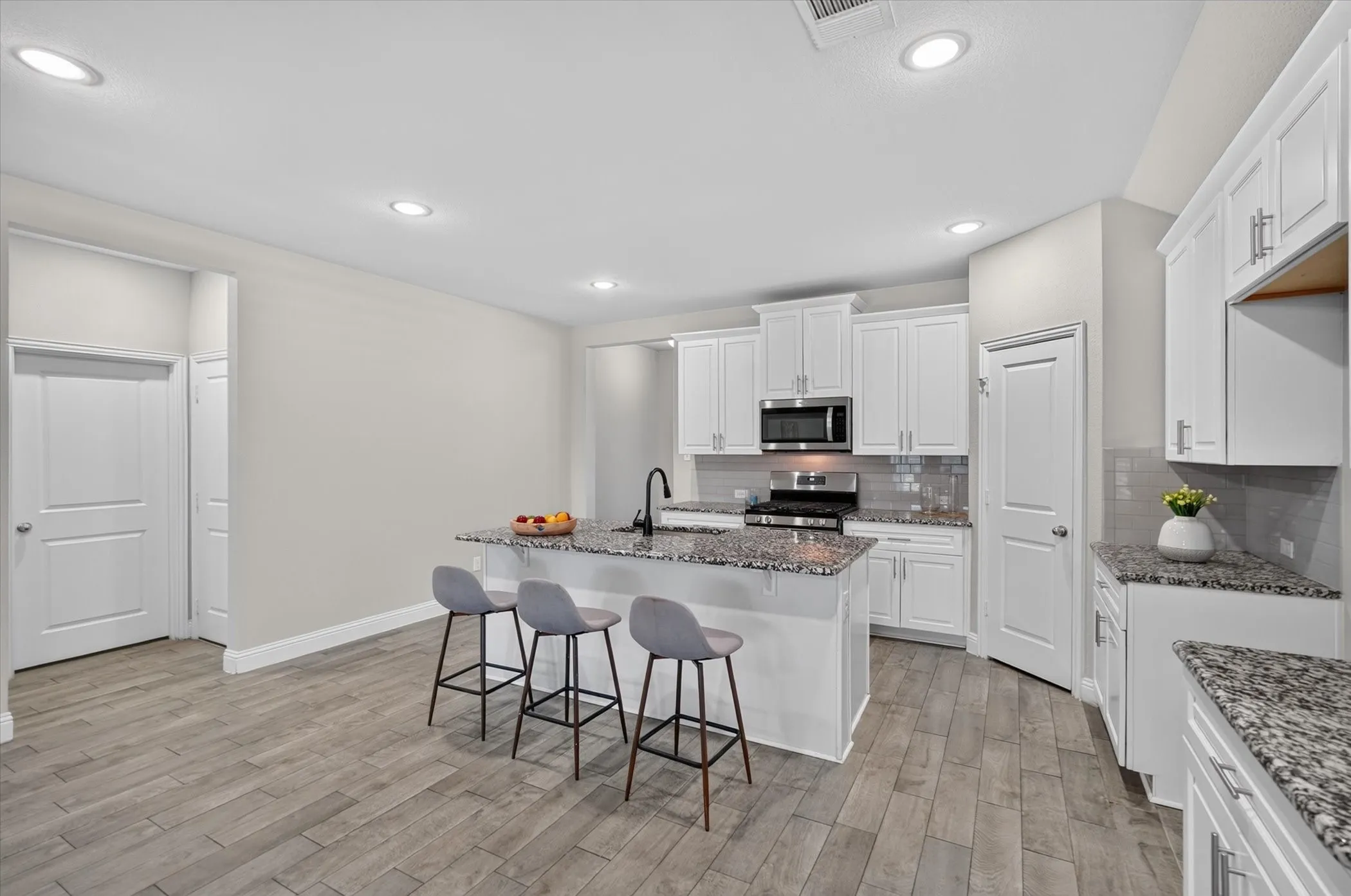 Open-concept kitchen featuring white cabinetry, stainless steel appliances, a tiled backsplash, a kitchen island with seating, and wood-finish flooring