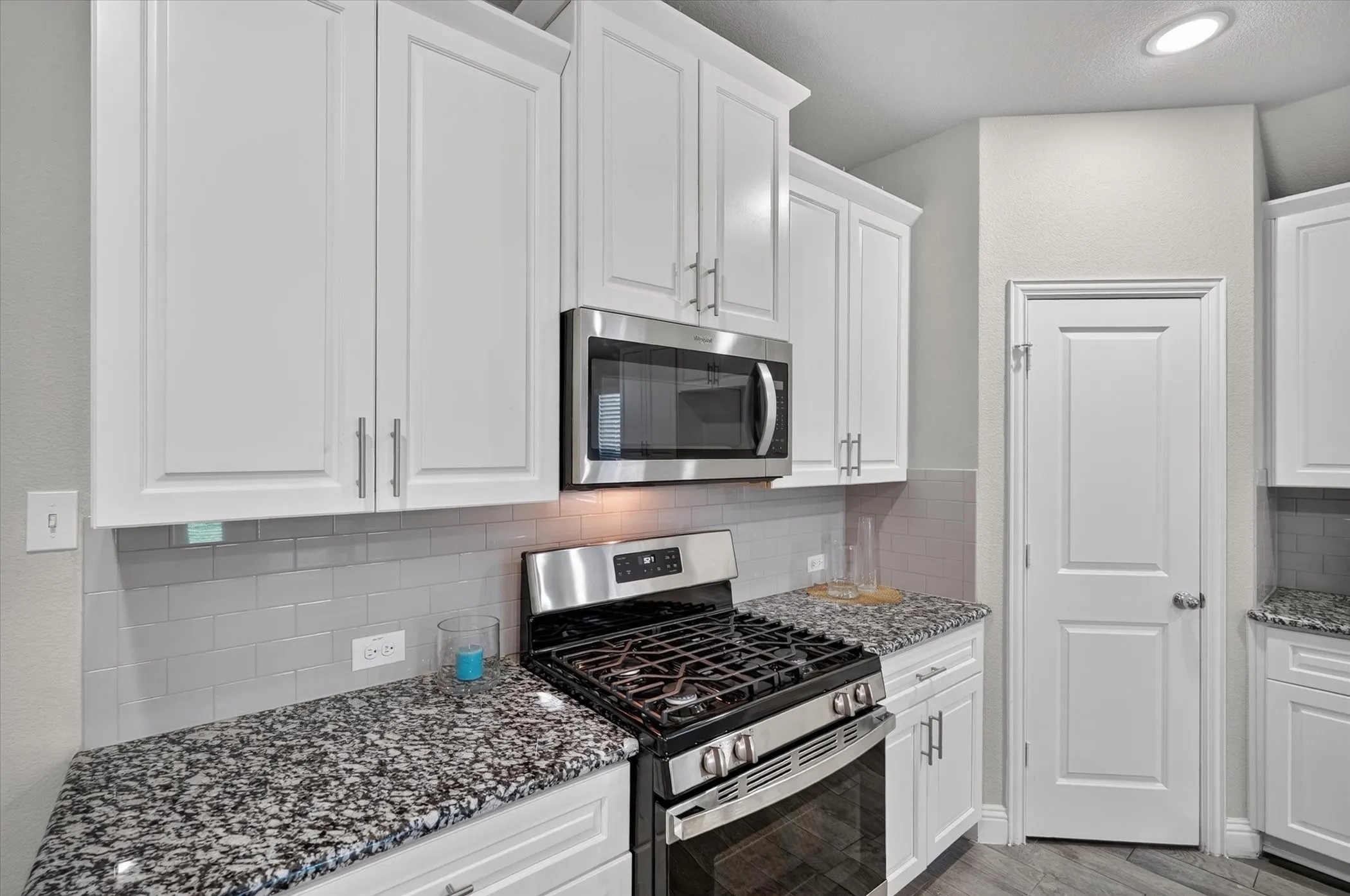 White shaker-style cabinetry with crown molding, stainless steel microwave, gas range, gray subway tile backsplash, and speckled countertops