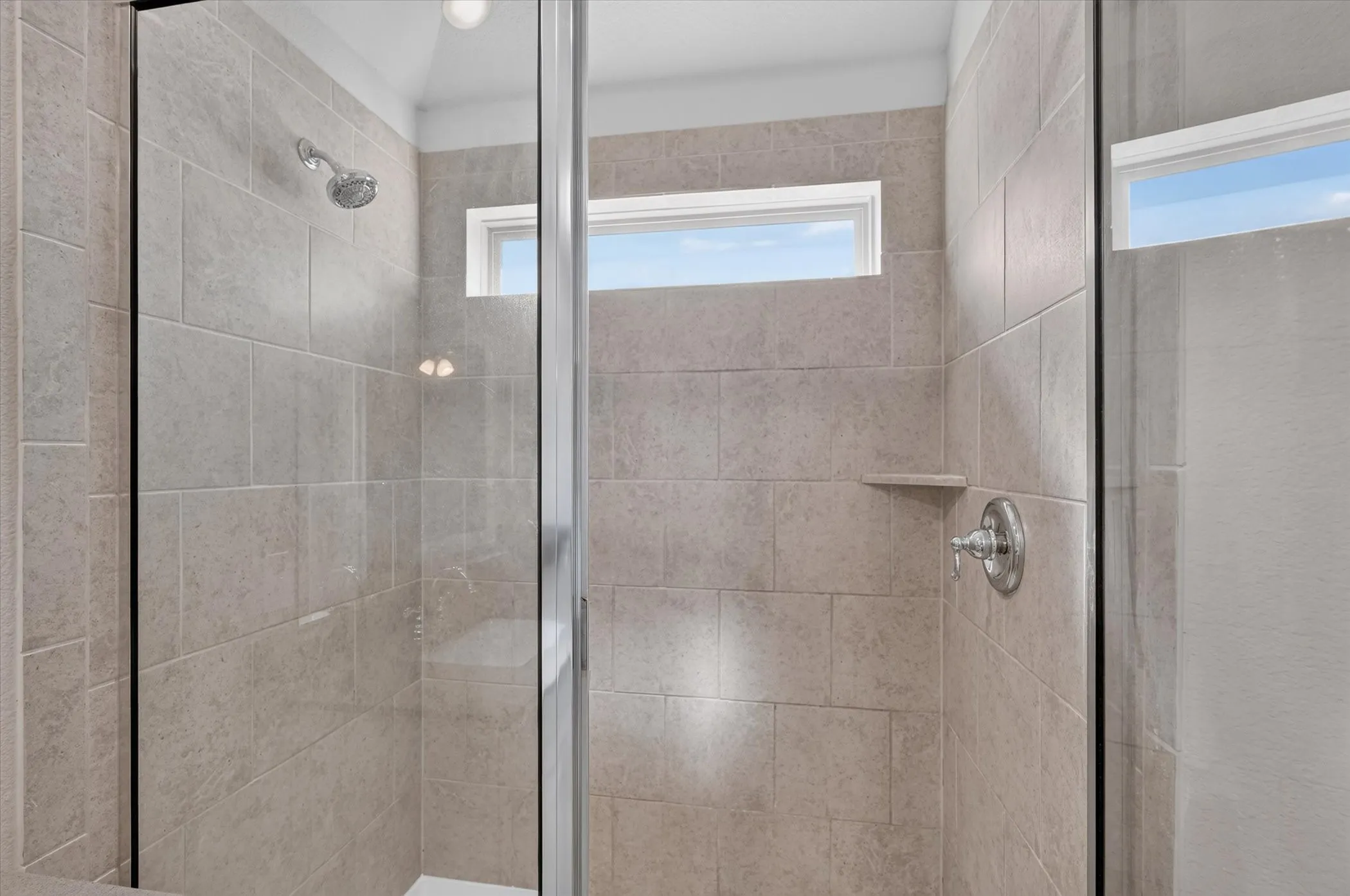 Spa-inspired shower featuring frameless glass enclosure, dual showerheads, built-in tile niche, and neutral tile surround with transom window for natural light