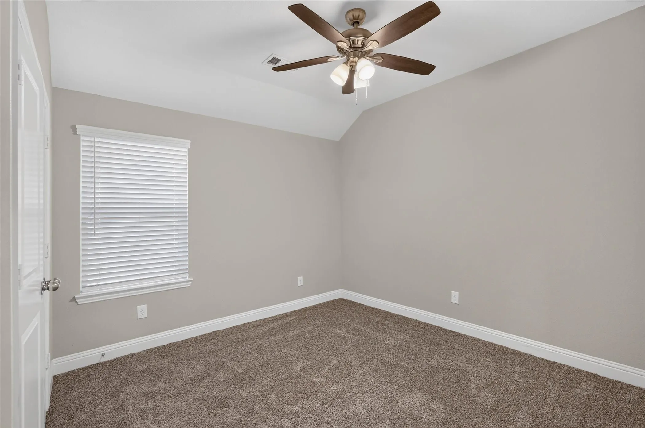 Spacious bedroom featuring neutral wall finishes, plush carpeting, ceiling fan with integrated lighting, and a large window with horizontal blinds providing natural light and privacy