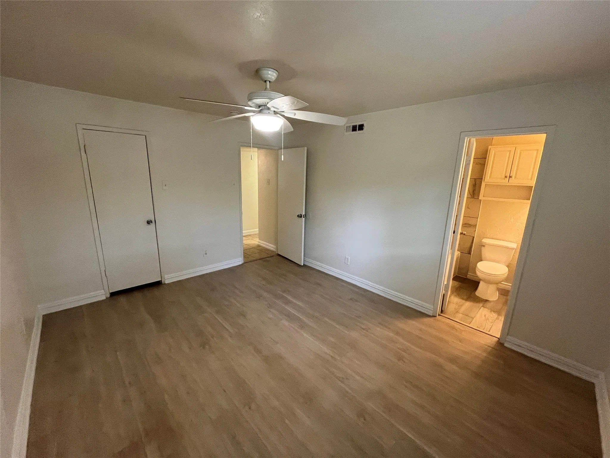 Wood-finish flooring with white baseboards, a white ceiling fan with integrated lighting, and a white interior door